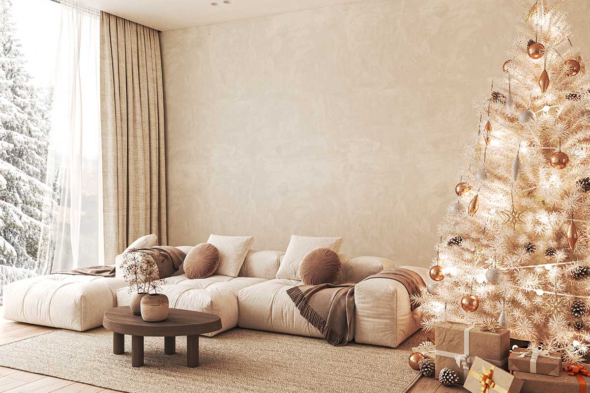 Soggiorno moderno con divano modulare chiaro, tavolino in legno, albero di Natale bianco decorato in oro e argento, grandi tende e vista sulla neve, palette neutra e luminosa.