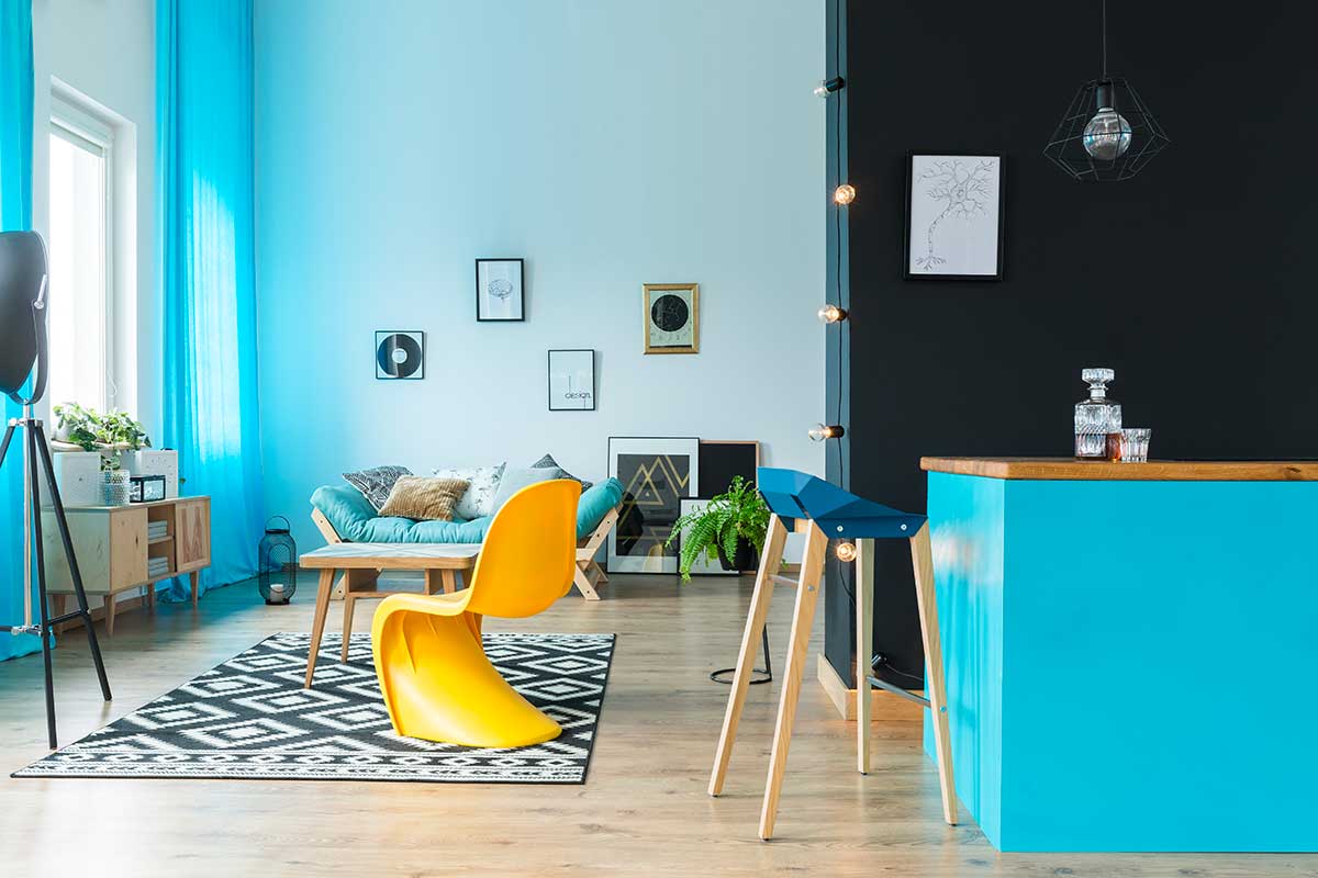 Soggiorno dal look pop con sedia gialla di design, parete nera, tende azzurre e tappeto grafico, colori vivaci e accenti contemporanei.