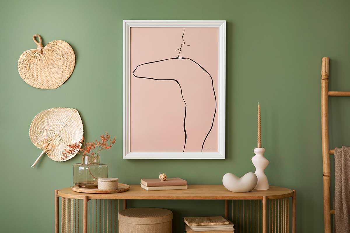 Parete verde salvia in soggiorno con decorazioni naturali: ventagli in vimini appesi, quadro minimalista con cornice bianca, consolle in legno chiaro, vasi e oggetti decorativi in toni neutri e beige. Atmosfera rilassata e contemporanea, stile naturale e luminoso.